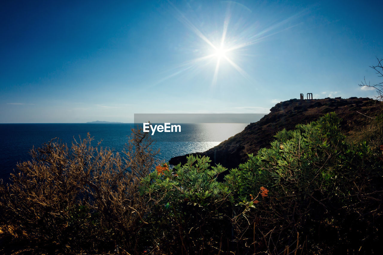 Scenic view of sun shining over sea and cliff