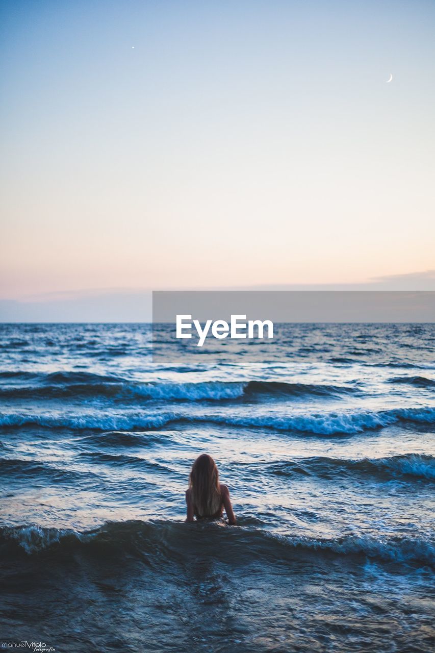 Rear view of woman sitting at beach against sky