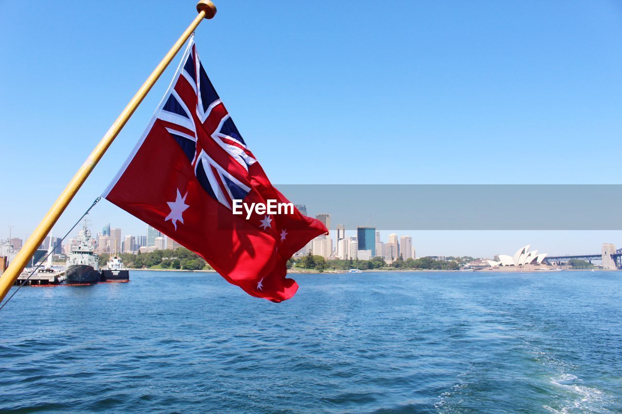 Red flag on river by buildings against sky