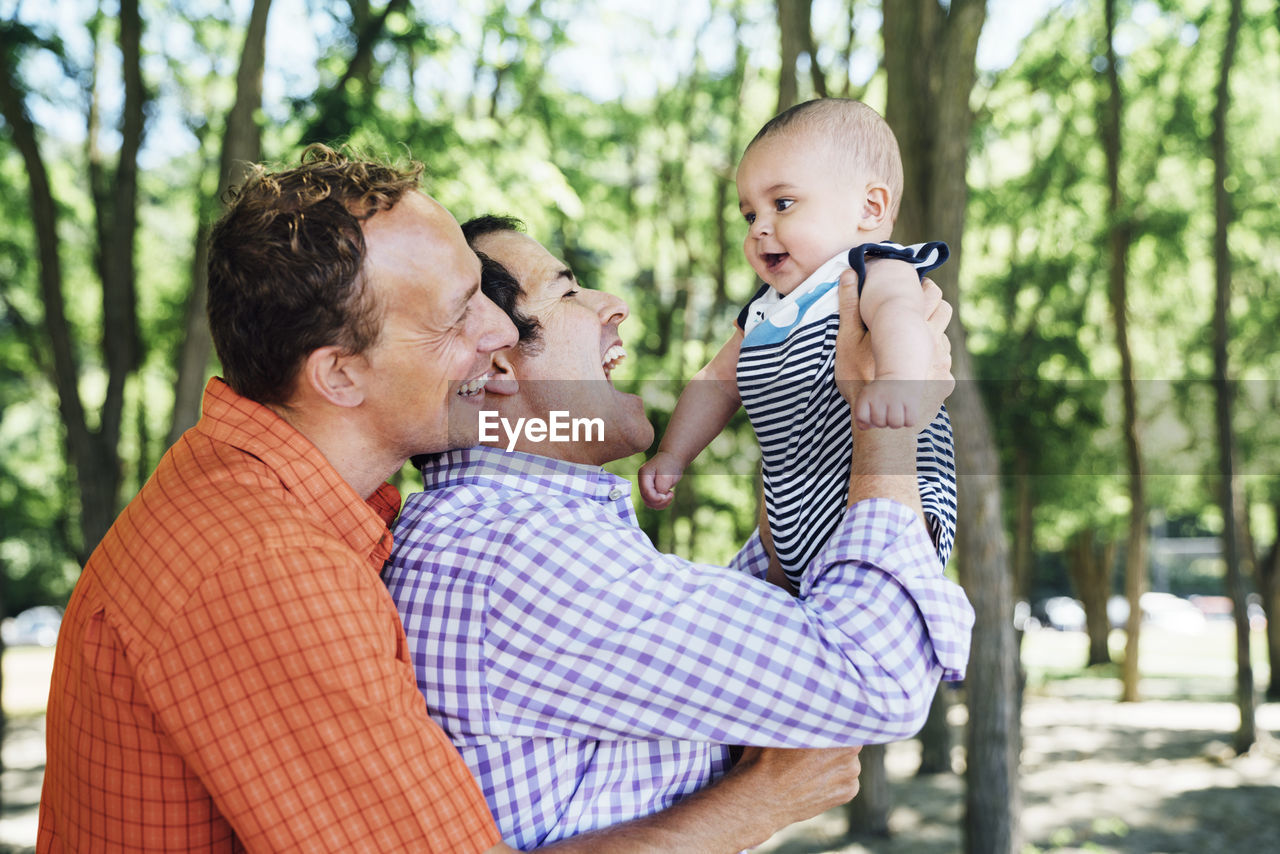 Smiling homosexual couple playing with baby boy at beach