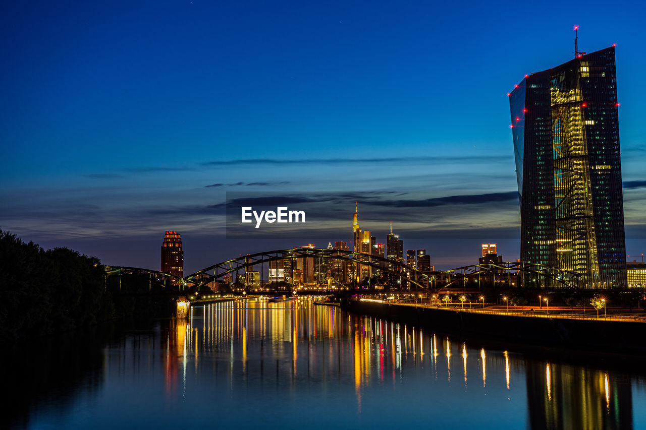 Illuminated buildings reflecting on river in city at dusk