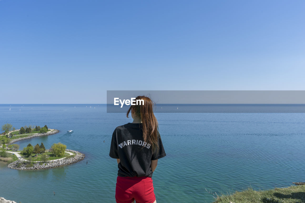 Rear view of young woman standing against sea