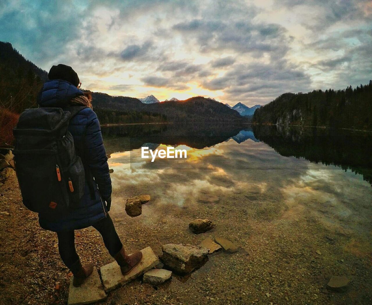 Rear view of man standing at lake against sky during sunset