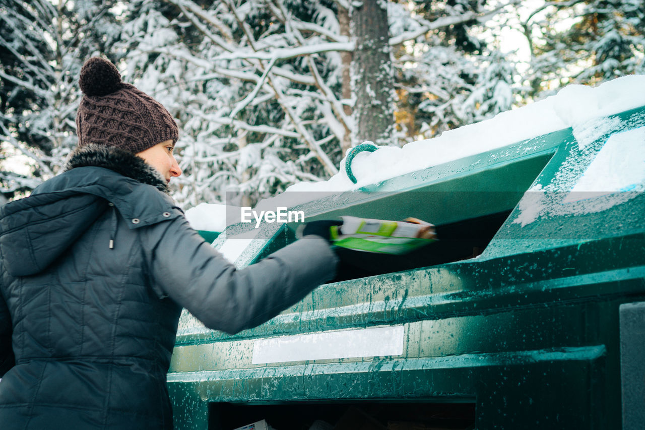 Rear view of woman putting garbage in can during winter