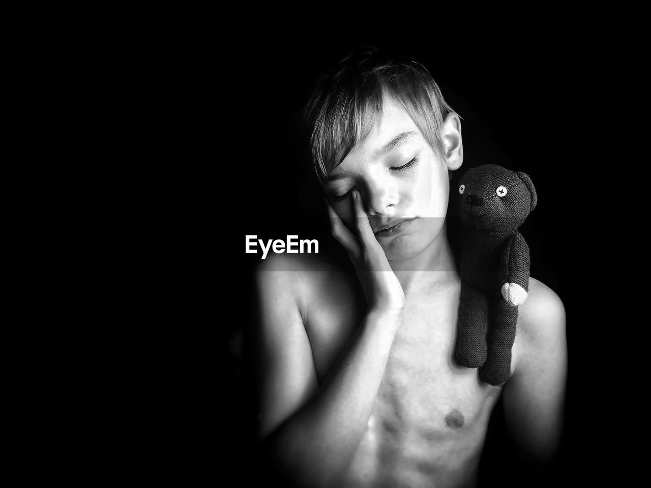 Shirtless boy with toy standing against black background