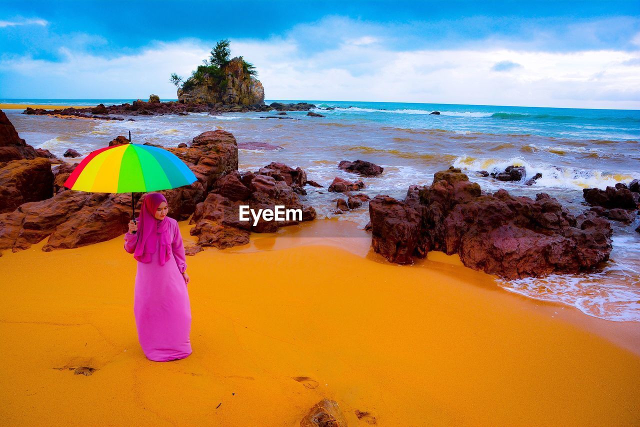 High angle view of woman with colorful umbrella standing at beach against sky