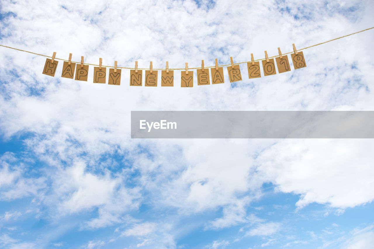 Low angle view of happy new year text hanging against cloudy sky