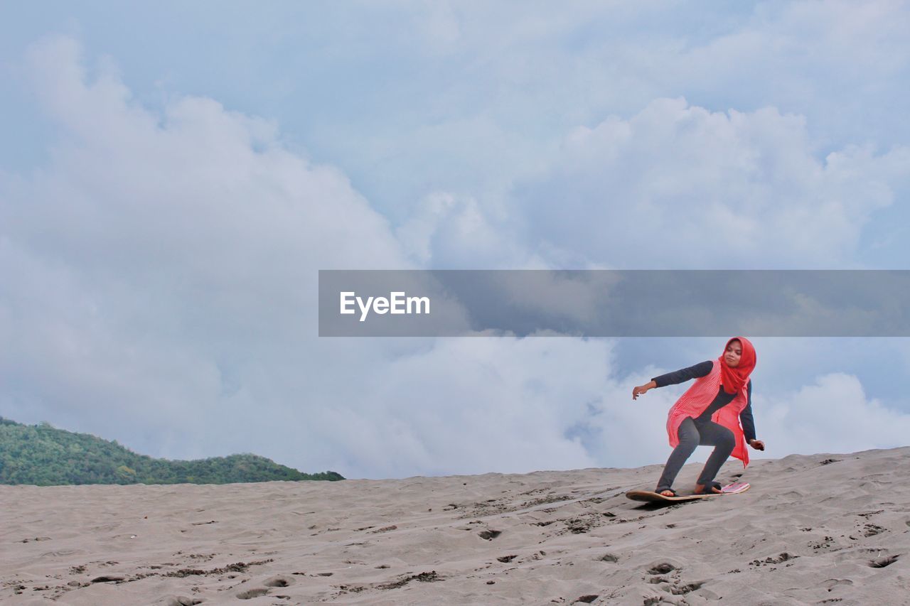 Low angel view of woman skateboarding on sand dune against sky