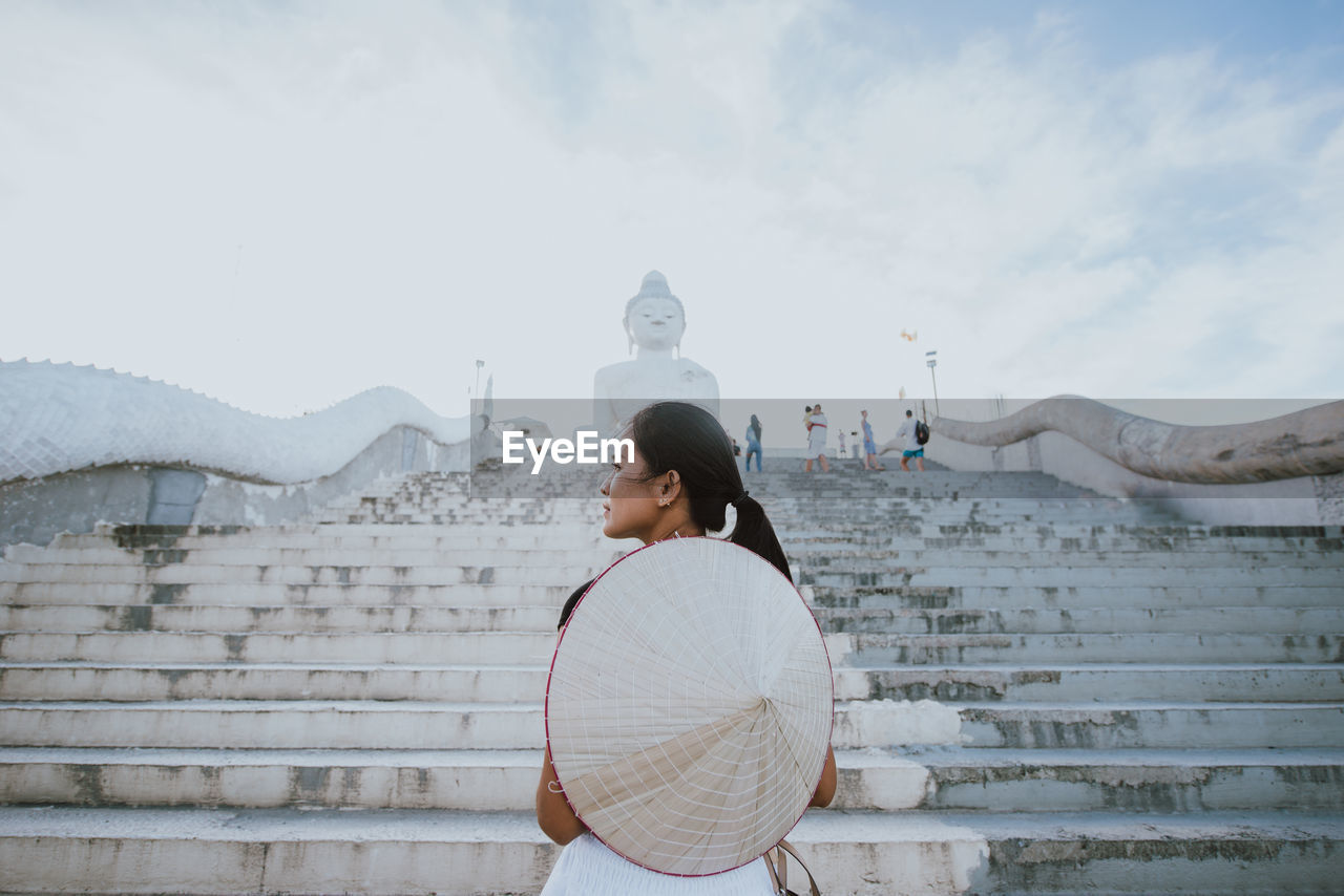 Rear view of woman standing against buddha statue and sky during winter