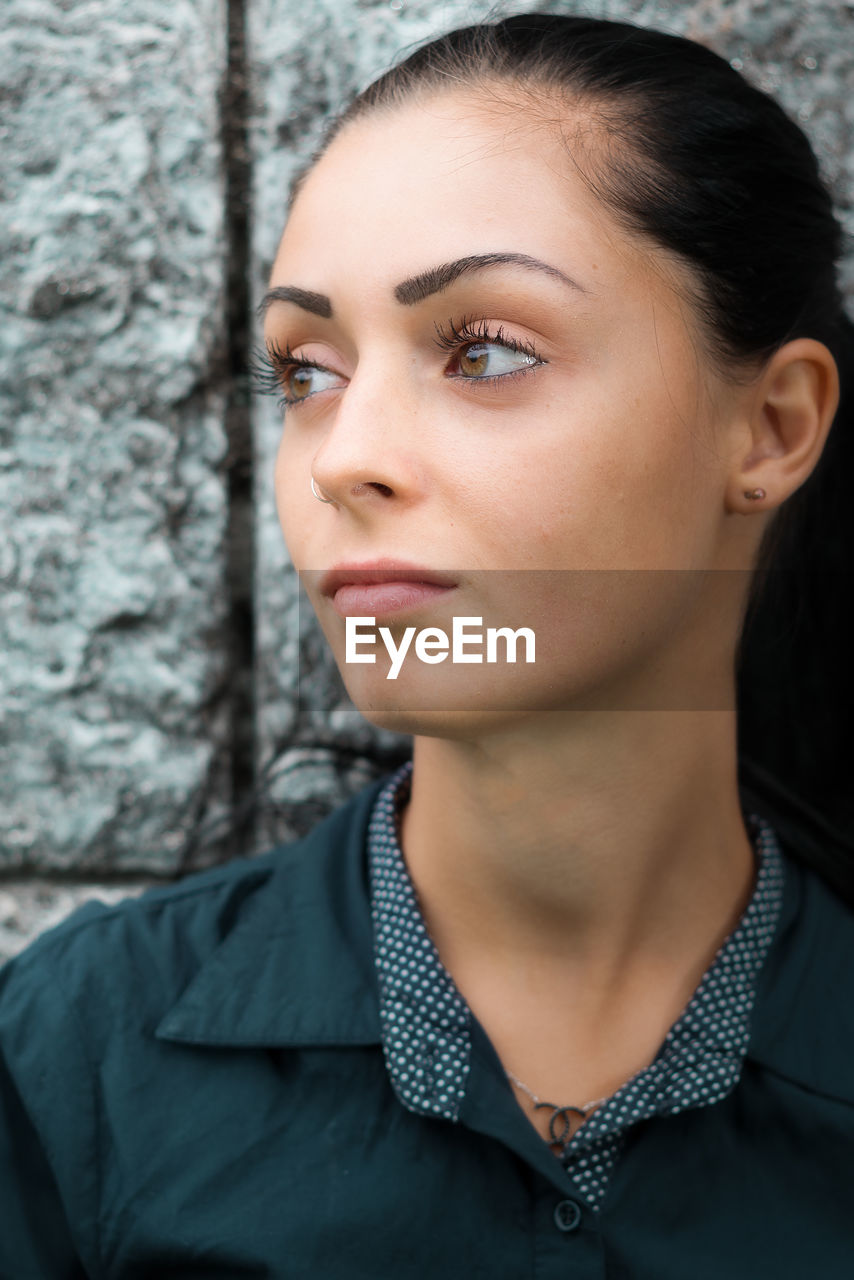 Close-up of young woman looking away against wall