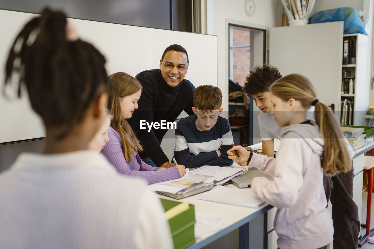 Happy teacher with multiracial students at desk in classroom