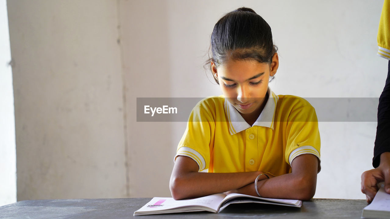 Portrait of happy indian school child sitting at desk in classroom, school kids with pens 