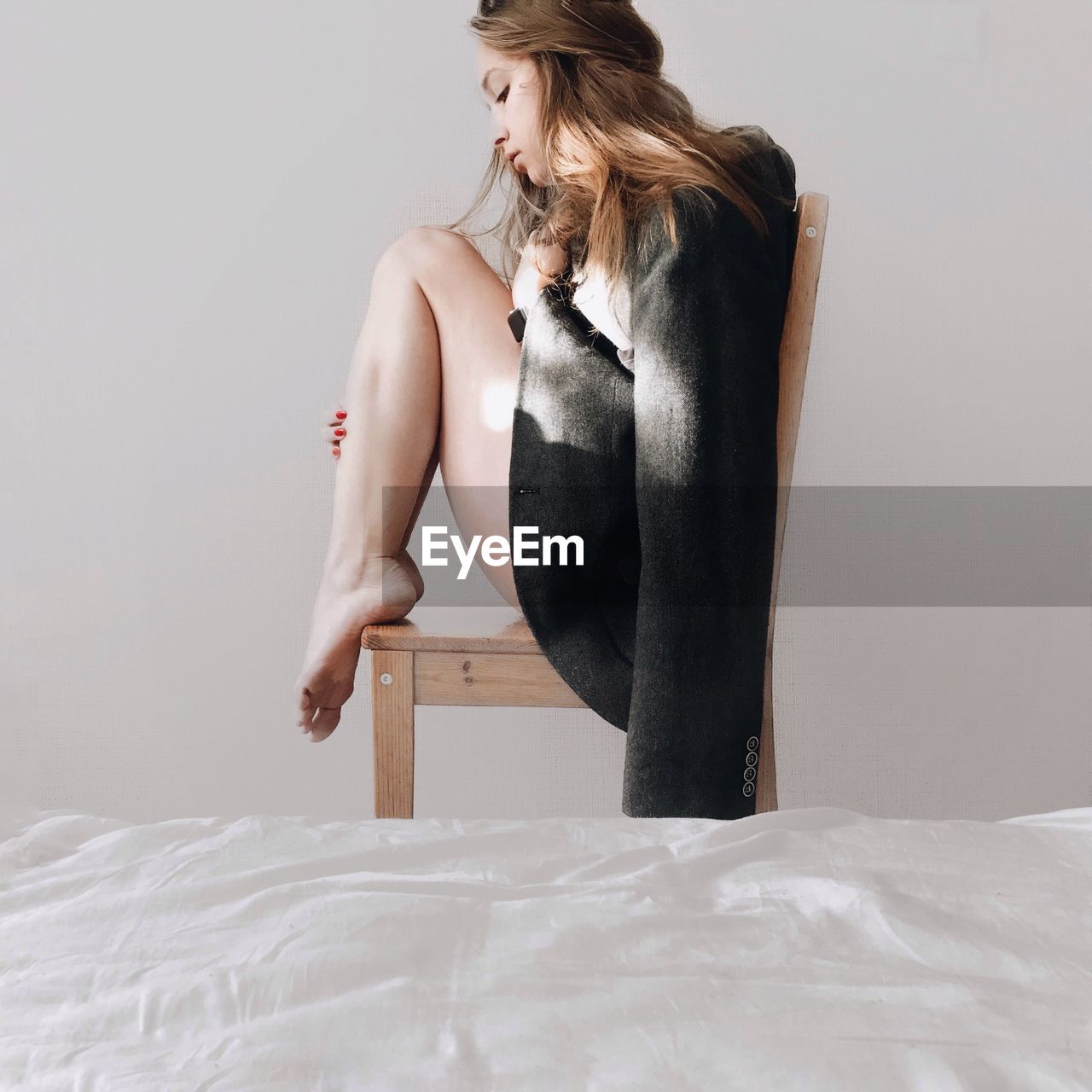 Woman sitting on chair at home against wall 