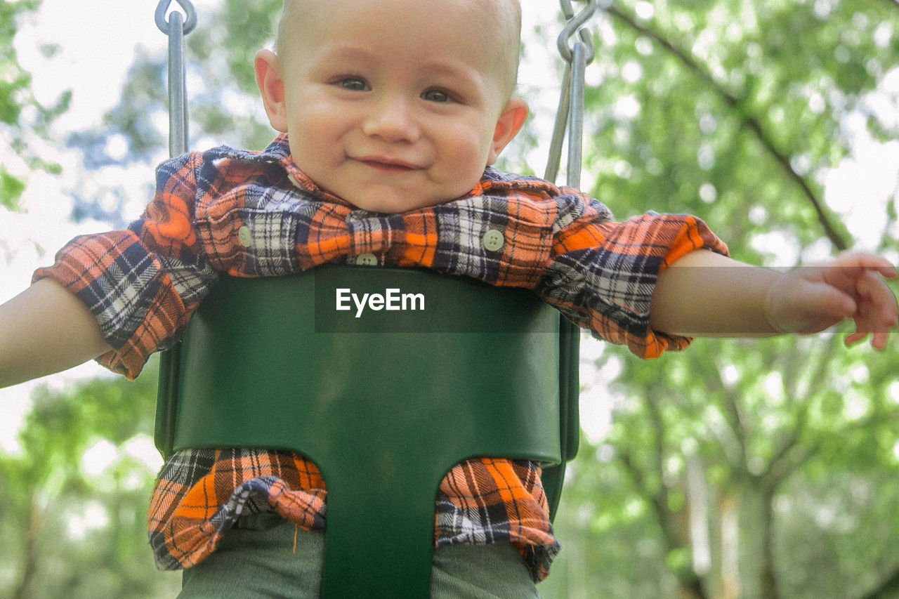 Close-up portrait of cute boy in swing at park