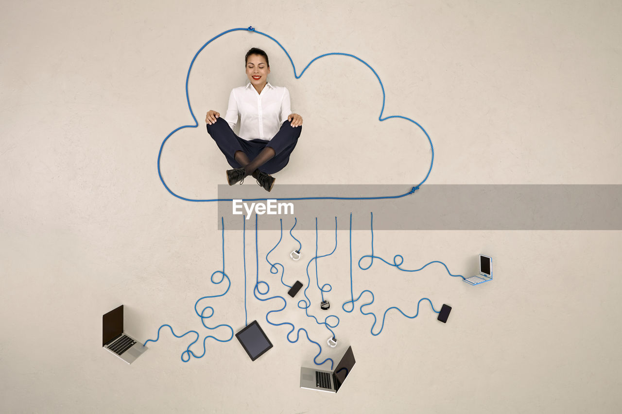 Businesswoman meditating in a cloud connected to mobile devices