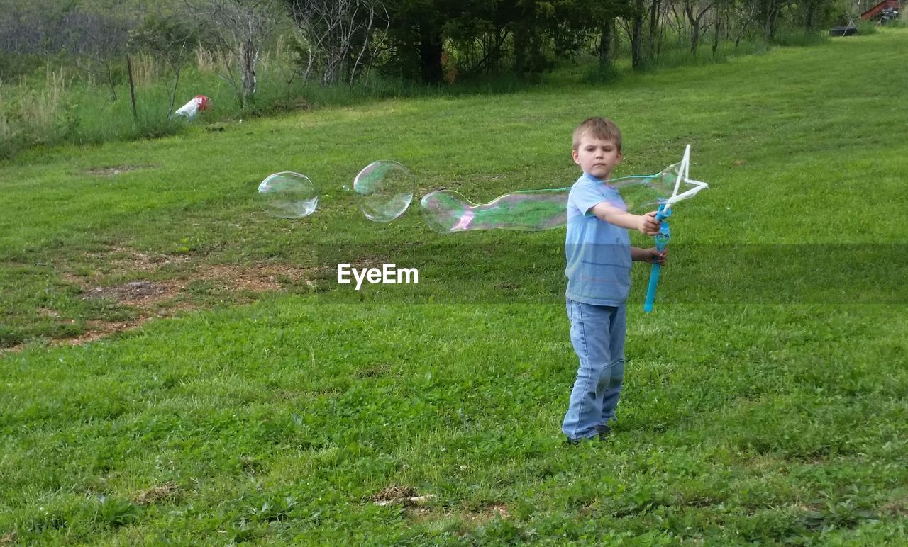 Full length of boy making bubbles on grassy land