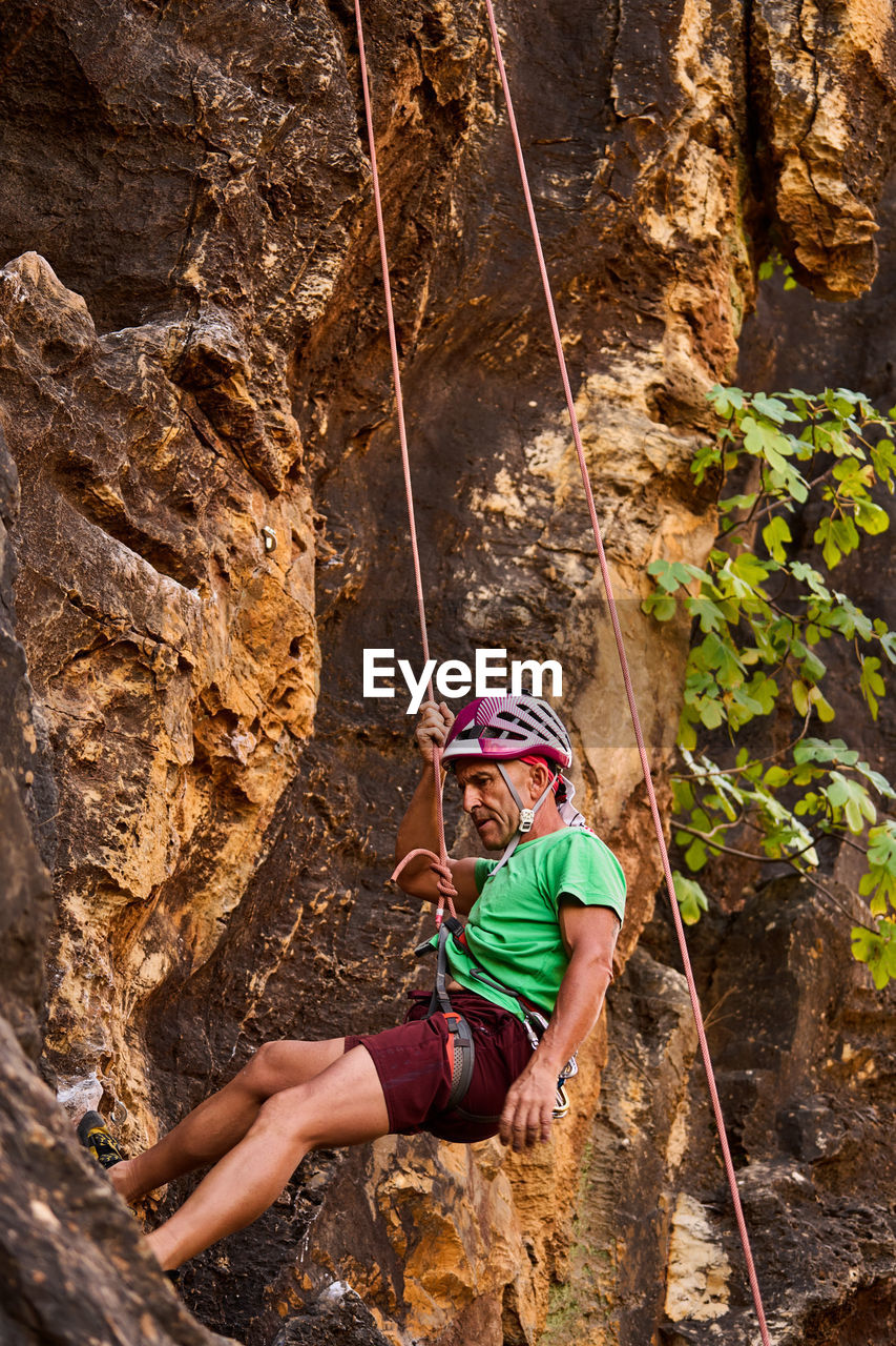 From below side view unrecognizable active fit senior man climbing on rocky cliff