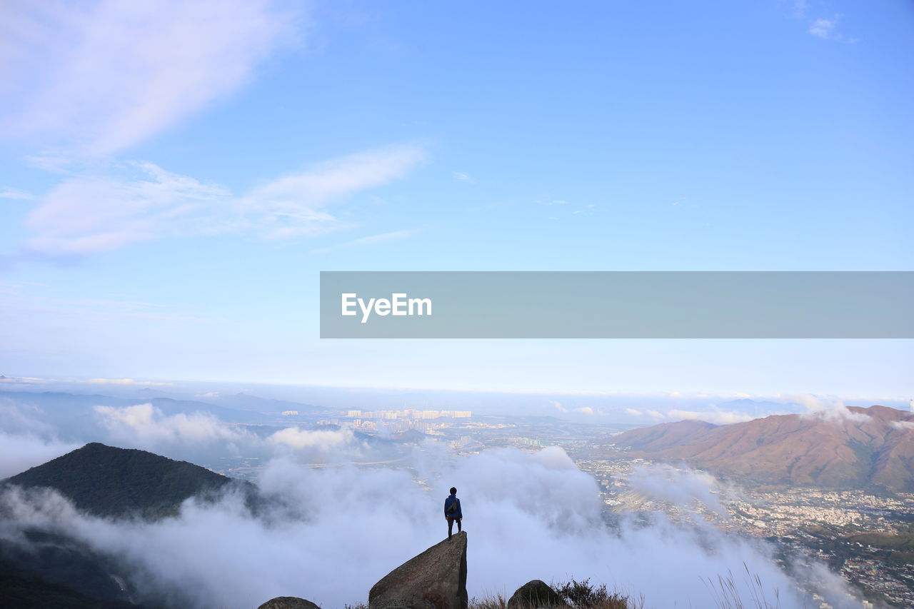 Rear view of man standing on rock against sky