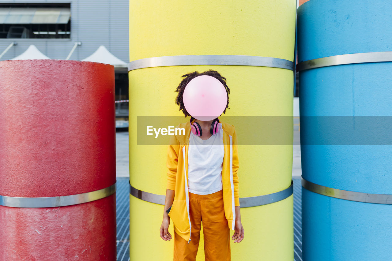 Young woman blowing bubblegum in front of colorful pipes