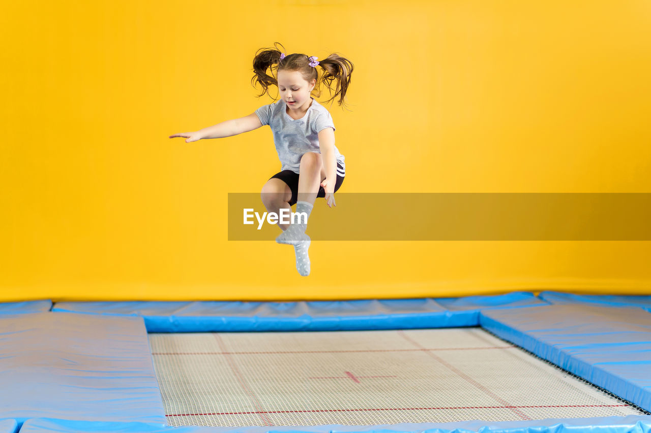 Full length of woman jumping against yellow wall