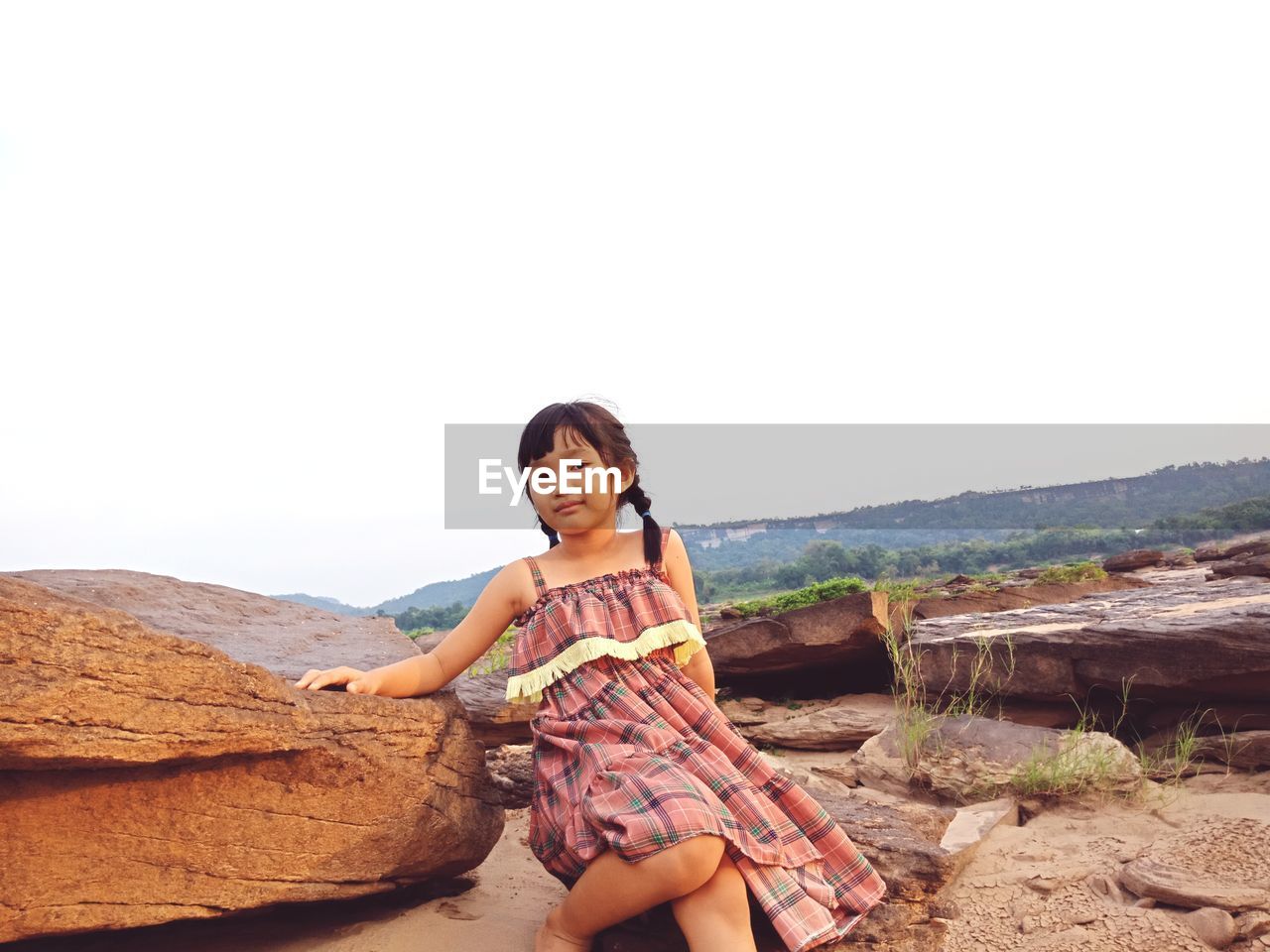 Portrait of girl sitting on rocks against clear sky