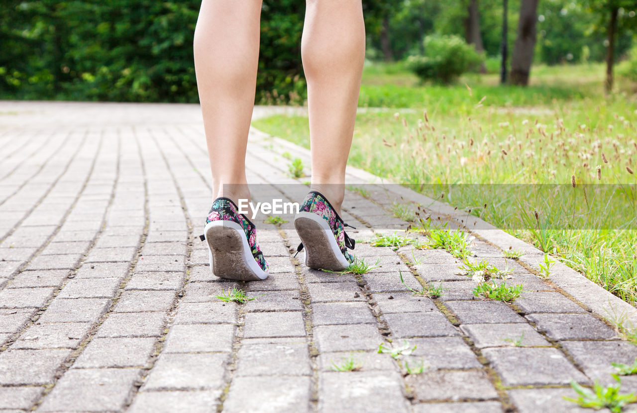 Low section of woman standing on footpath at park