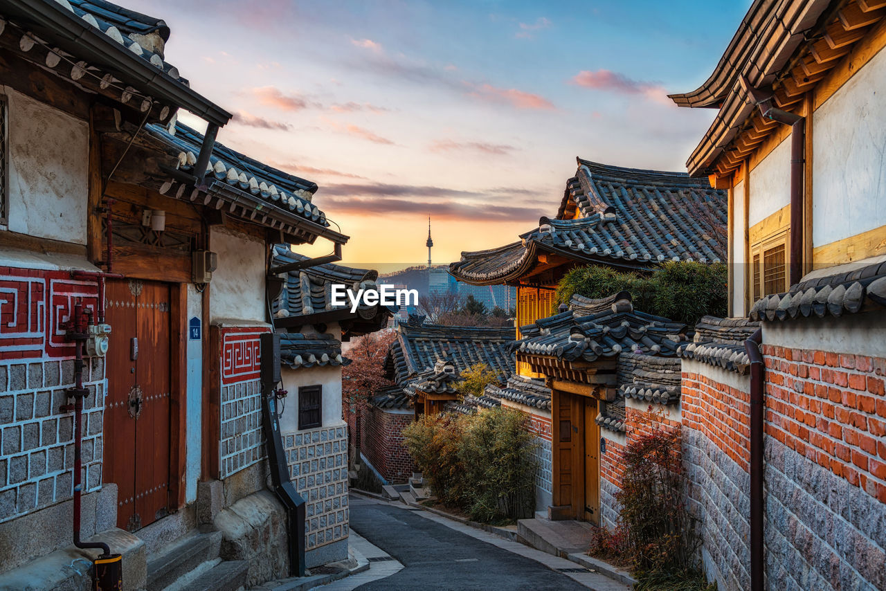 Street amidst buildings in city against sky during sunset