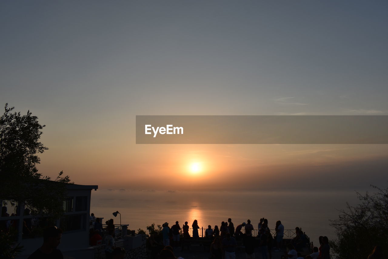 sky, sunset, group of people, large group of people, crowd, evening, nature, silhouette, dusk, water, sea, beauty in nature, horizon, sun, tree, leisure activity, architecture, lifestyles, beach, scenics - nature, plant, land, men, women, travel destinations, outdoors, orange color, sunlight, adult, travel, cloud, vacation, holiday, trip, tourism, idyllic