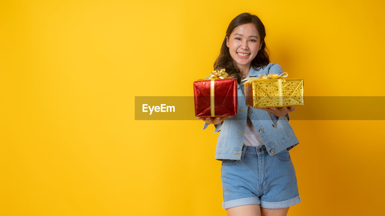 PORTRAIT OF A SMILING YOUNG WOMAN AGAINST YELLOW COLORED BACKGROUND