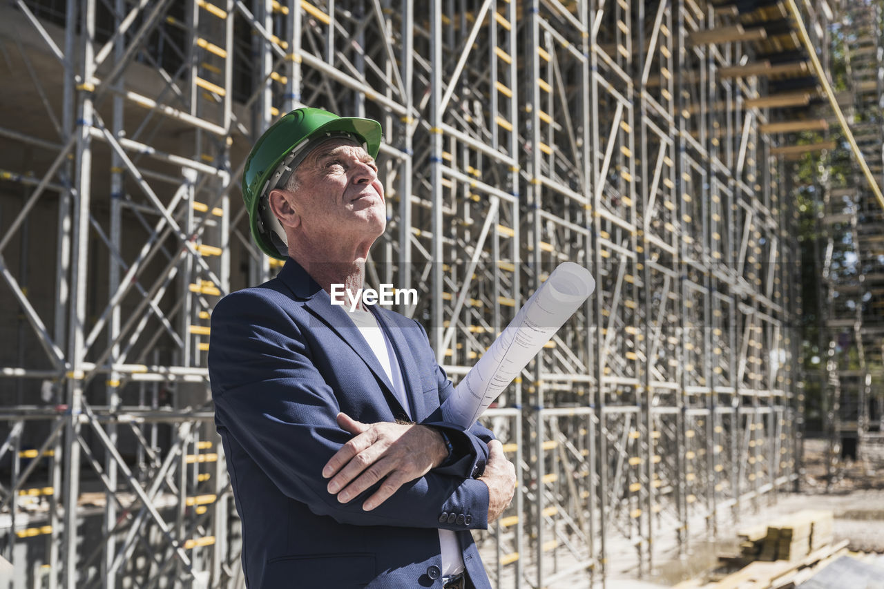 Thoughtful architect with blueprint at construction site