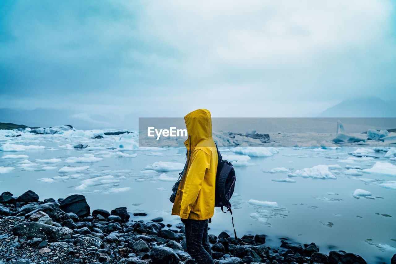 Woman standing on snow covered shore against sky