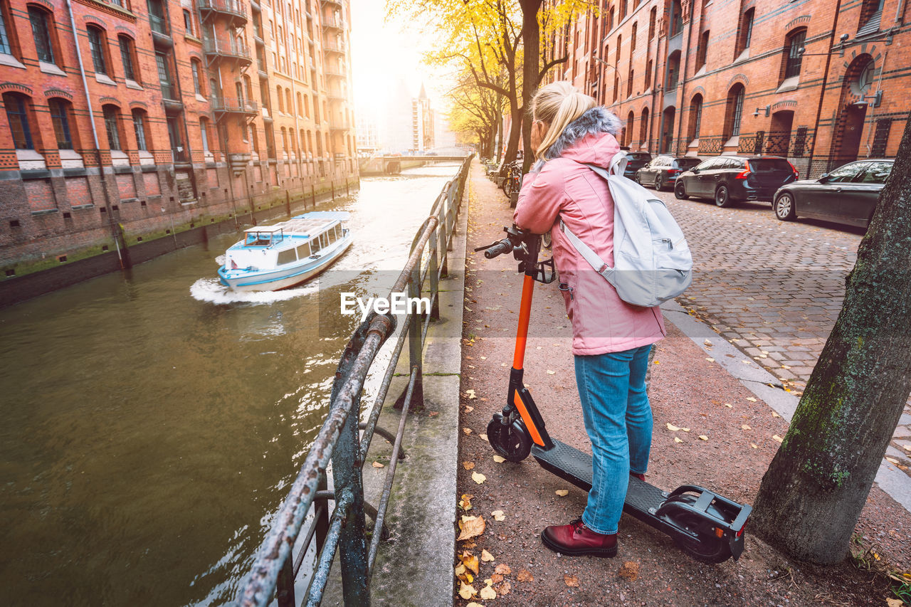 Rear view of woman with push scooter on footpath