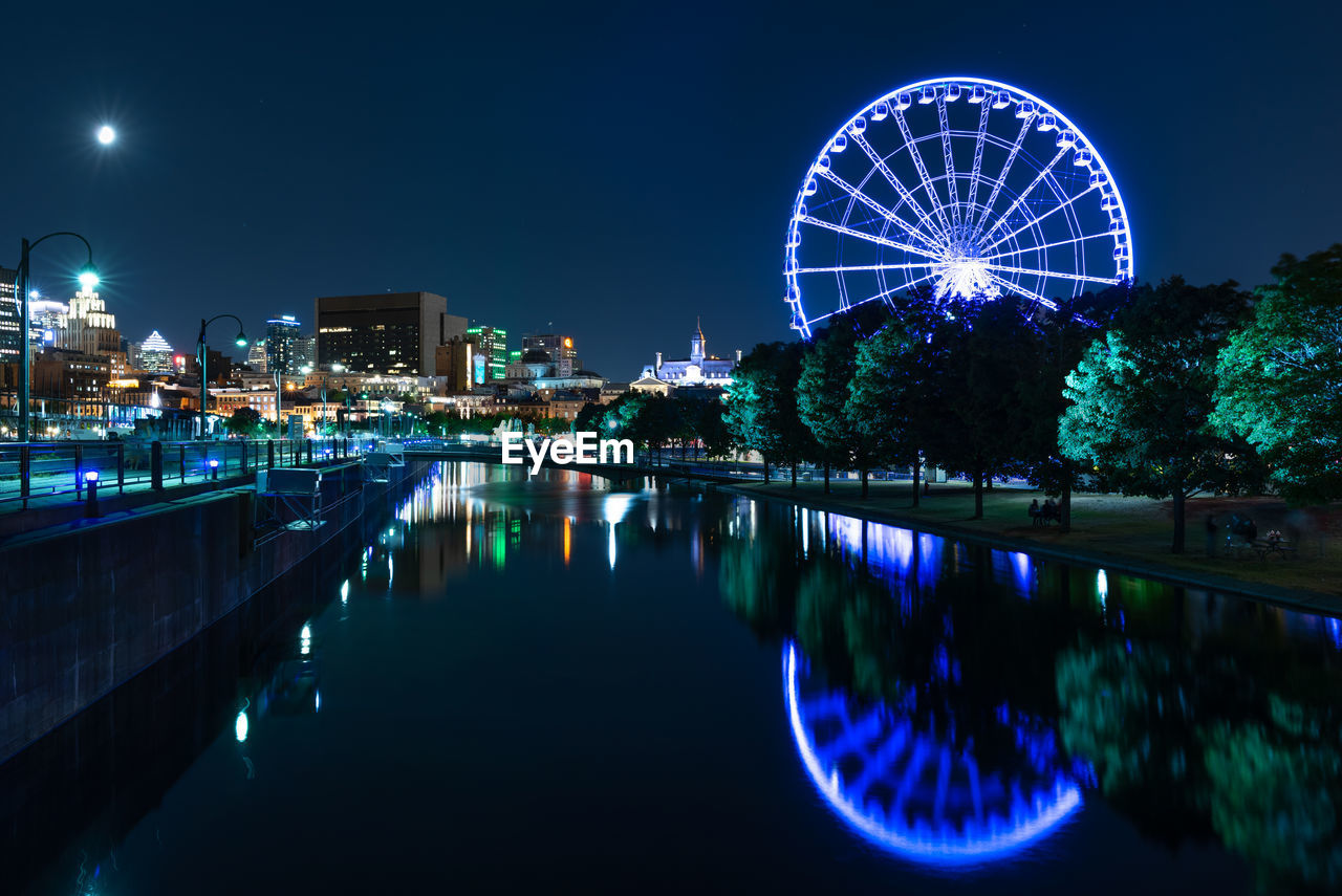 ILLUMINATED FERRIS WHEEL BY RIVER AT NIGHT