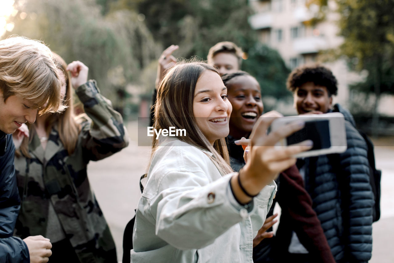 Happy multi-ethnic friends taking selfie with mobile phone on street in city