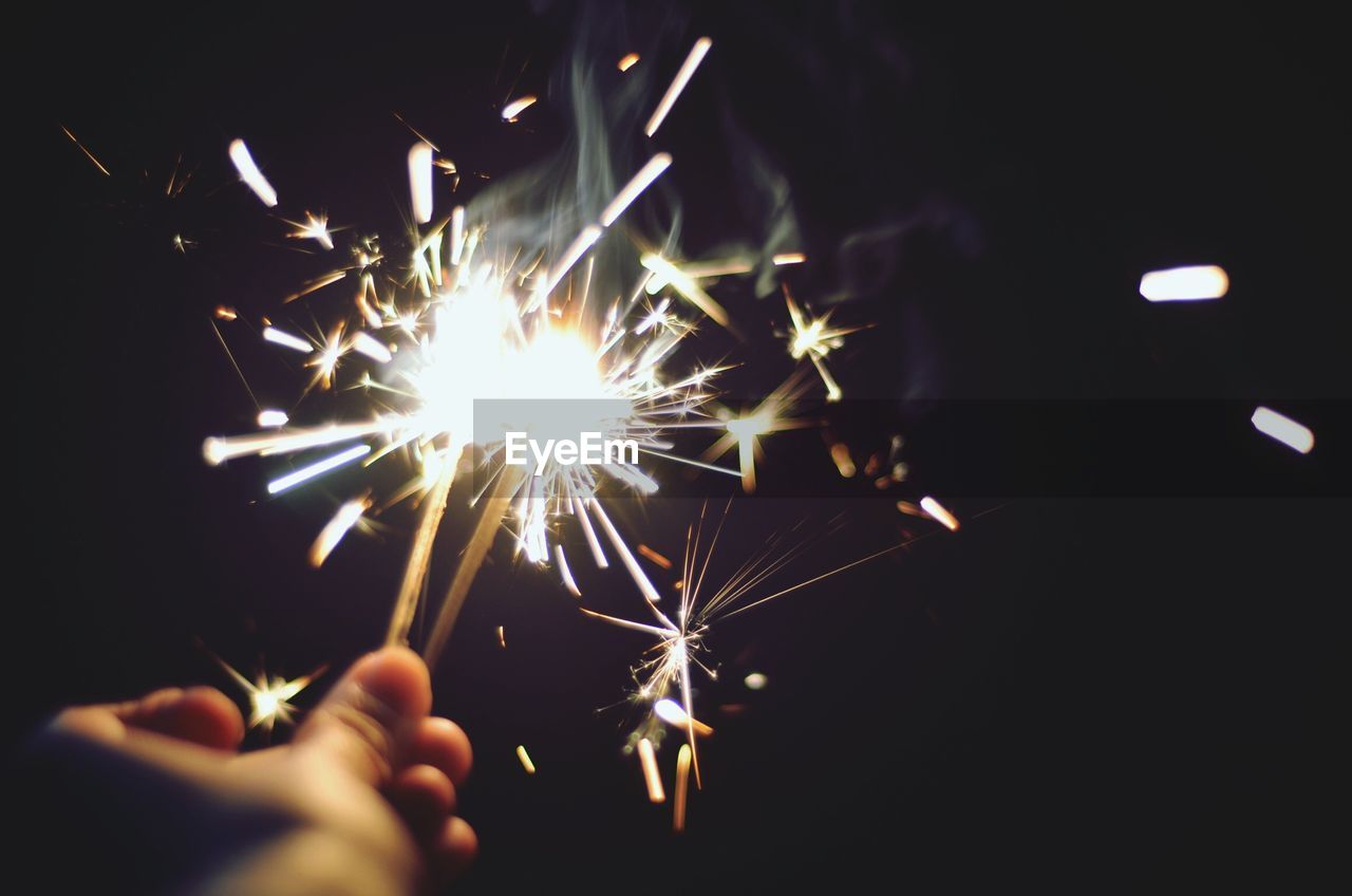 Cropped image of hand holding sparkler at night