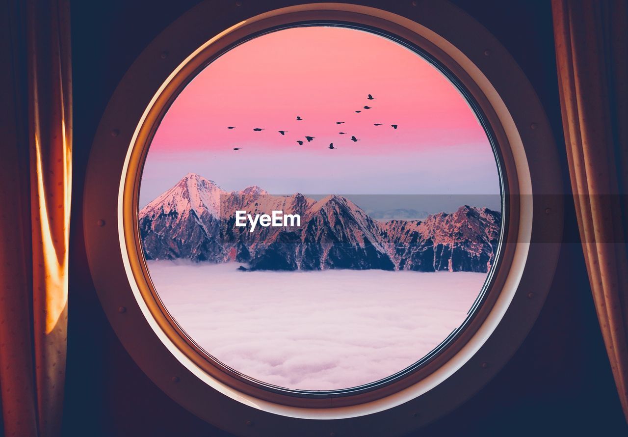 Snowcapped mountains and clouds seen through circle shaped window