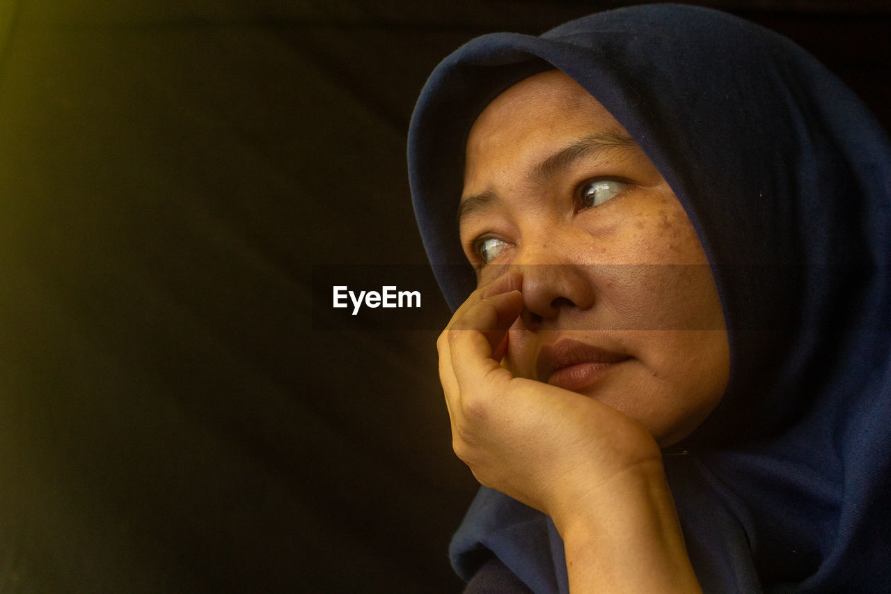 portrait, headshot, one person, adult, person, headscarf, serious, looking, human face, religion, female, contemplation, clothing, copy space, indoors, women, emotion, human head, belief, hat, close-up, spirituality, hood, looking away, sadness, hood - clothing, lifestyles, young adult, hijab, praying
