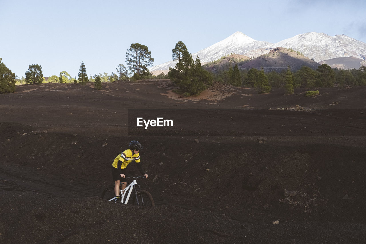Female cyclist riding bike on dirt road with snowy mount teide in back