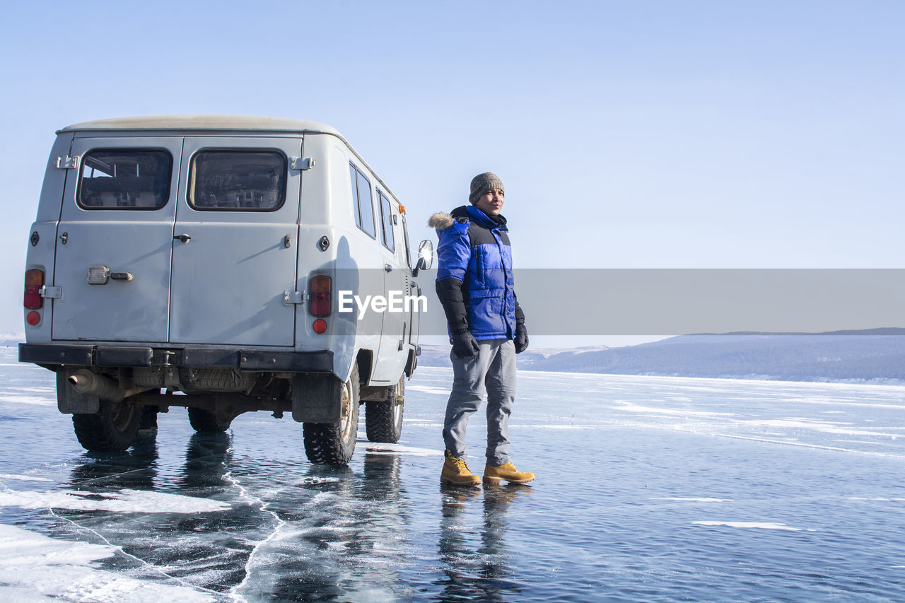 Man standing by van on frozen lake against sky