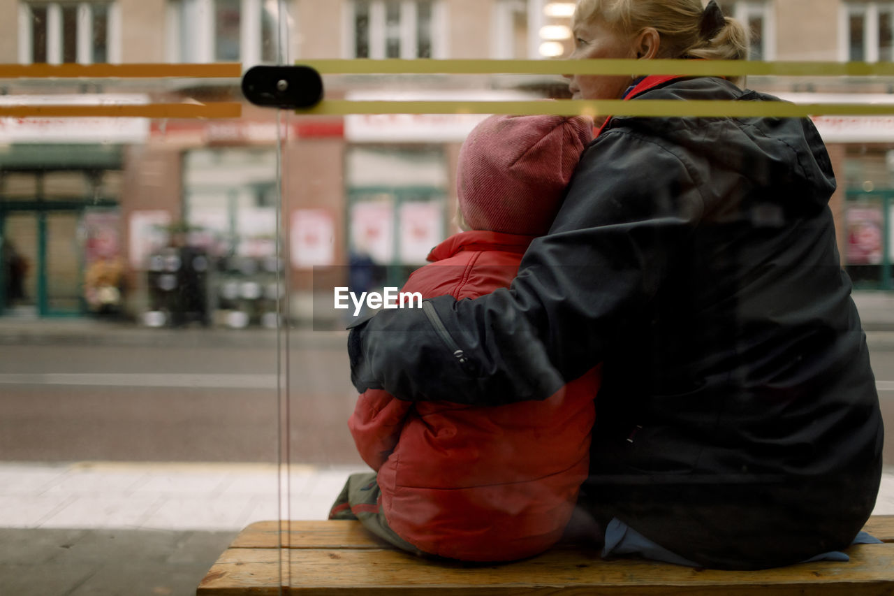 Rear view of grandmother with grandson sitting on bench in city