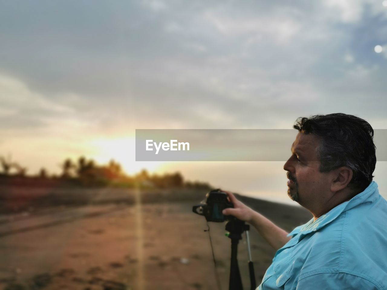 MAN PHOTOGRAPHING AT CAMERA AGAINST SKY