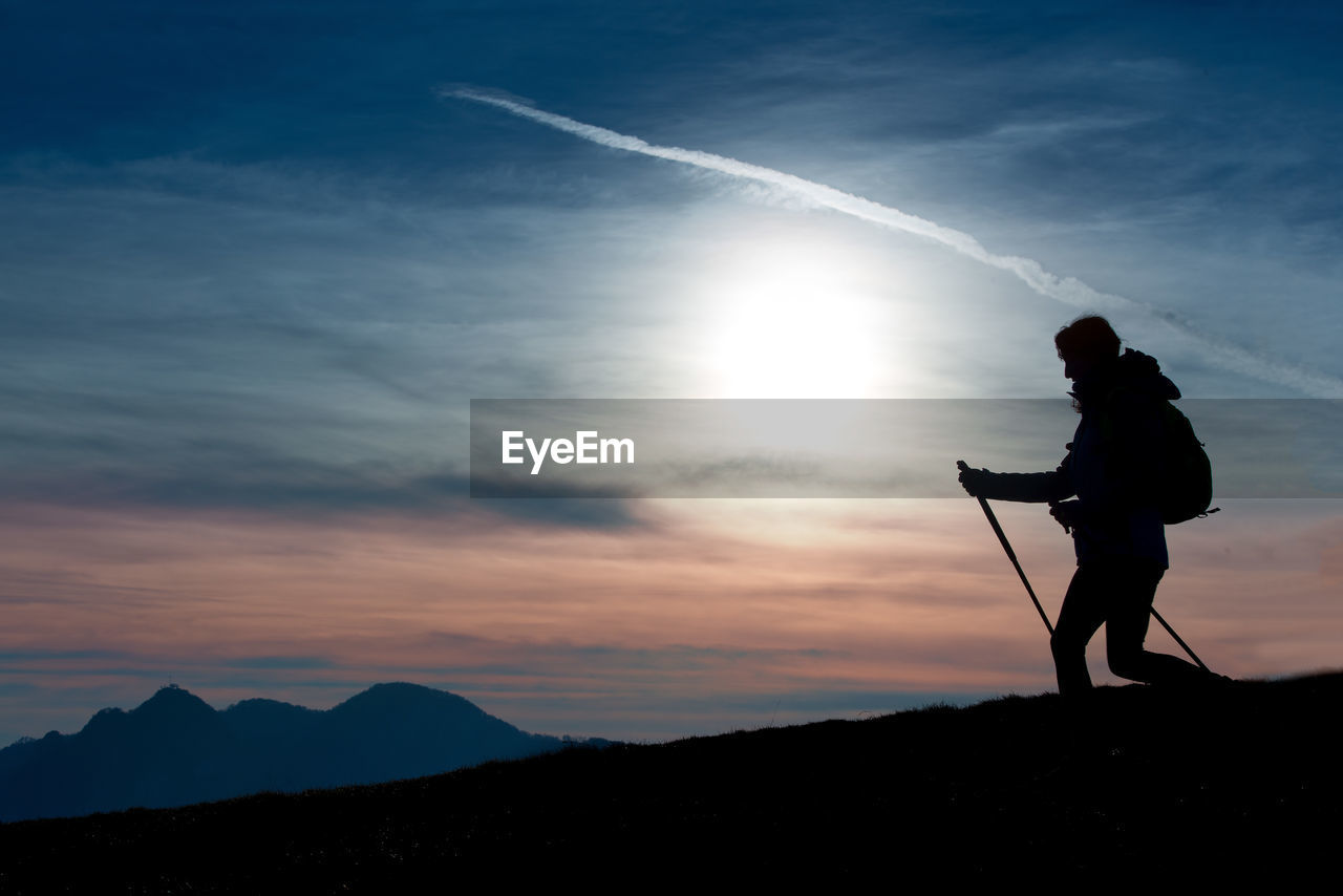 Silhouette of a girl on a mountain during a religious trek in a blue and orange sky..