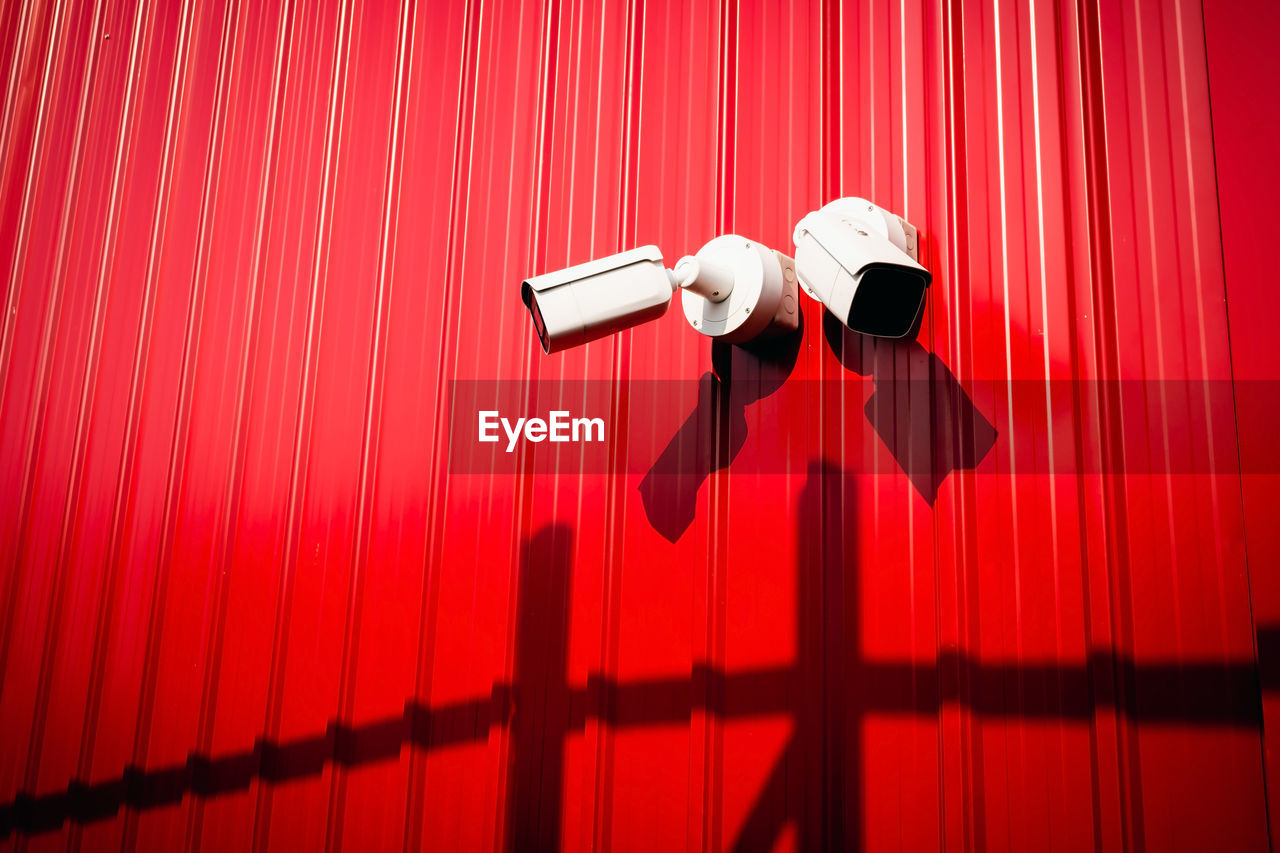 A low angle view of a cctv camera against a red wall