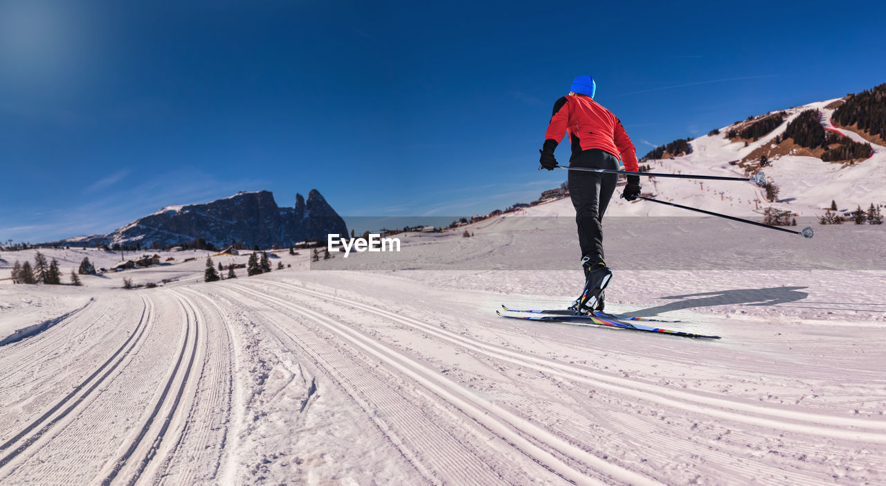 REAR VIEW OF MAN SKIING ON SNOWCAPPED MOUNTAIN AGAINST SKY