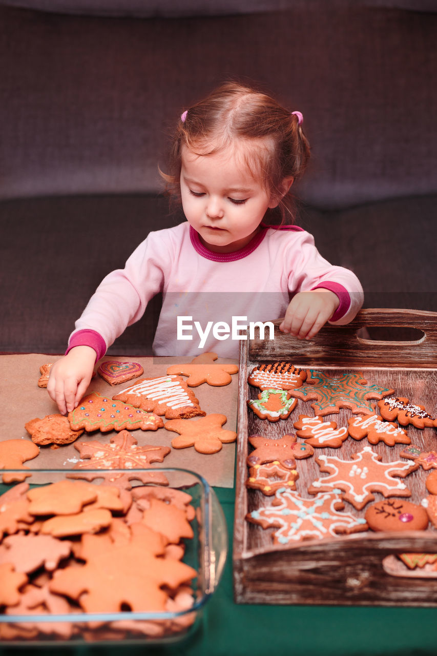 Girl arranging christmas gingerbread cookies in wooden tray at home