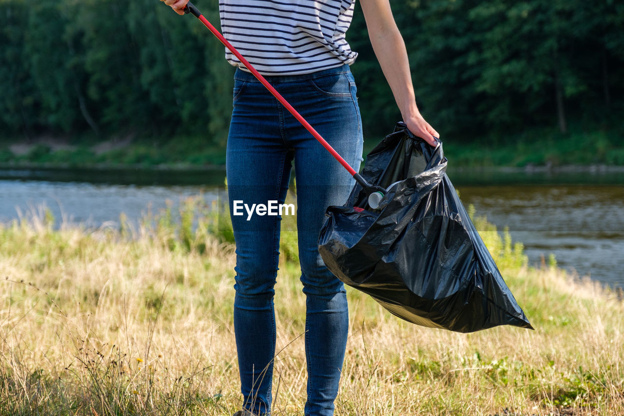 Midsection of woman collecting garbage on land against river