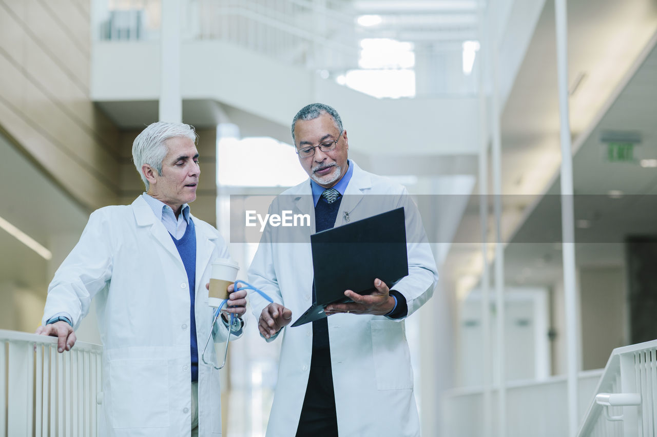 Male doctors discussing over laptop computer in hospital corridor