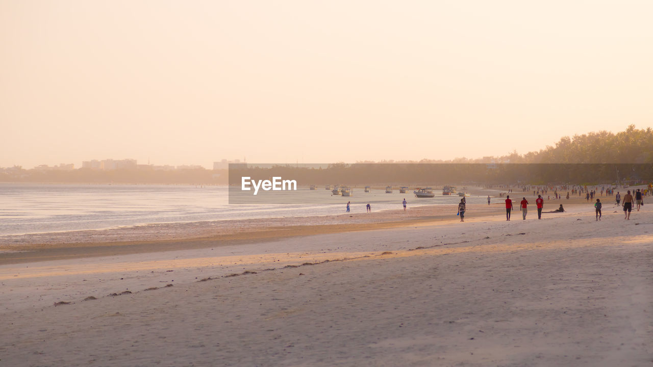 Group of people on beach against clear sky during sunset