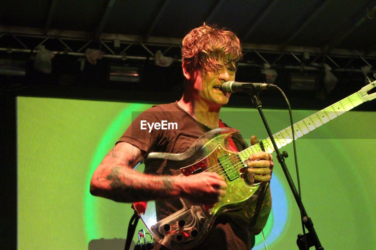 Low angle view of mature musician playing guitar at stage in nightclub