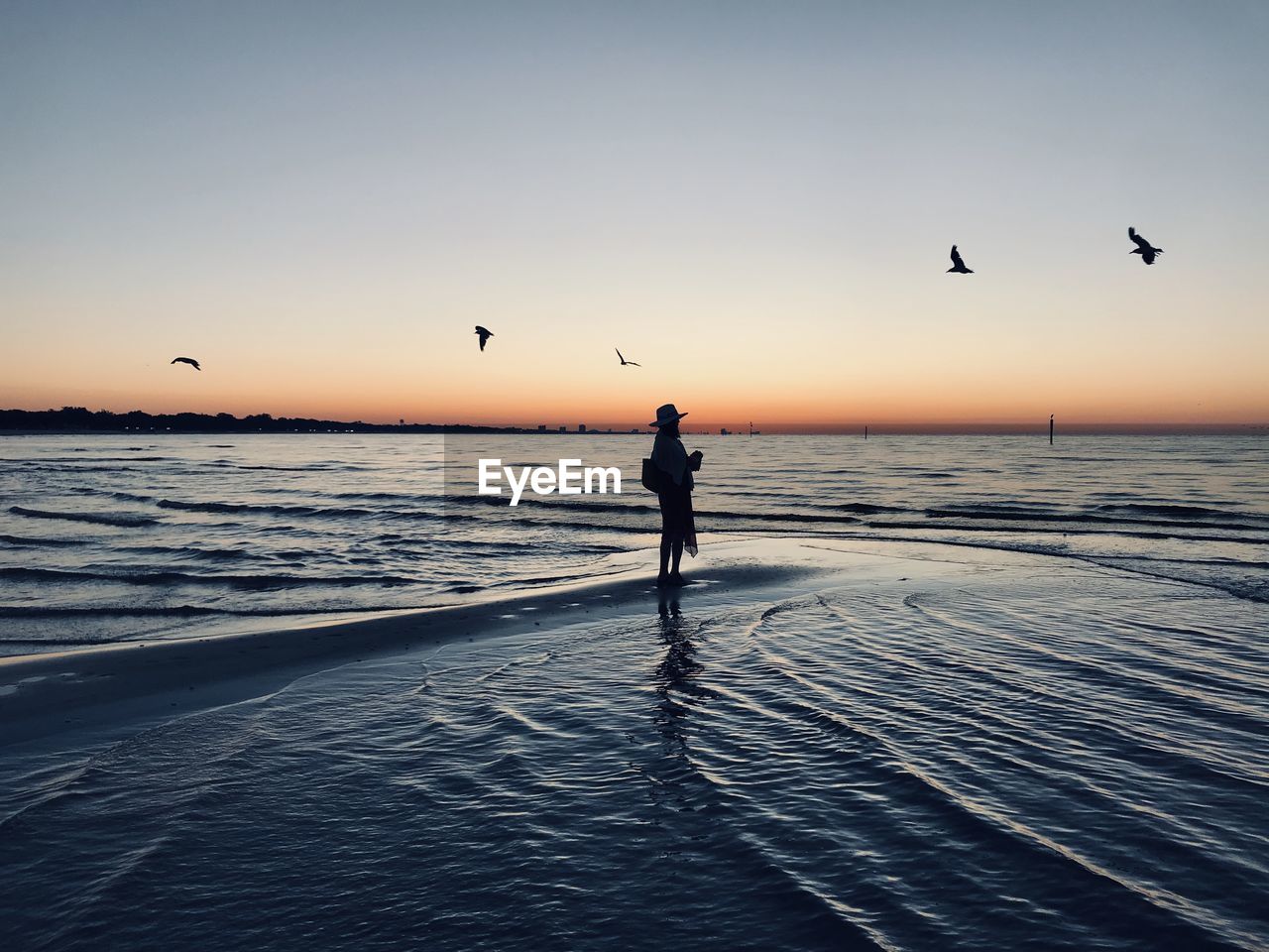 Silhouette woman standing in sea against clear sky during sunset